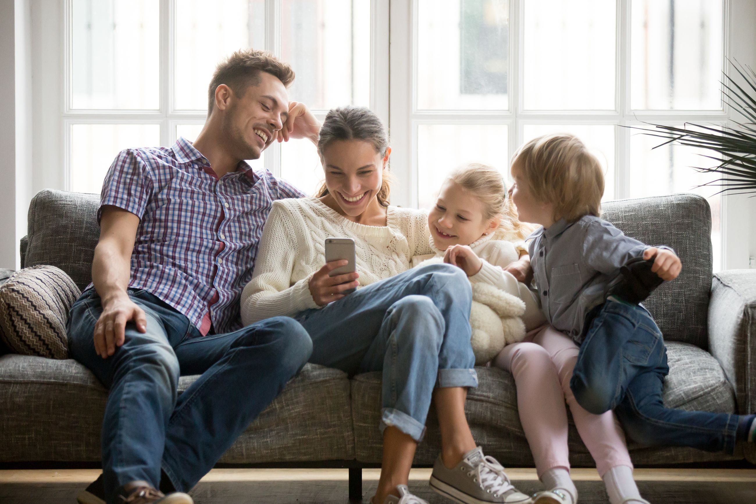 Familie mit zwei Kindern sitzt auf einem Sofa und schaut gemeinsam auf ein Smartphone